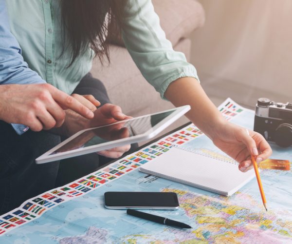 Two people planning an international trip together with a map, tablet, and notebook